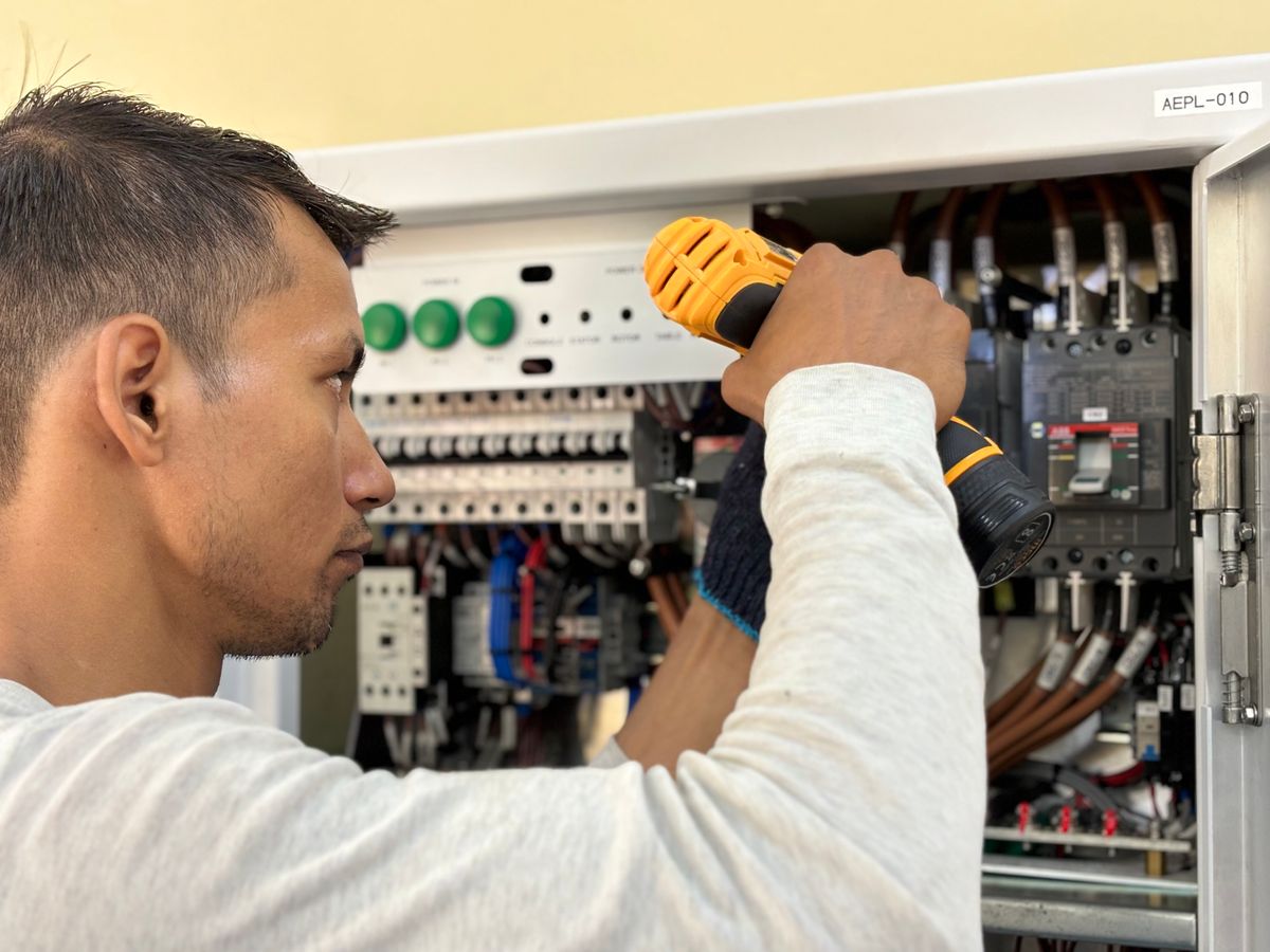 Electrician working on an indoor electrical panel with a drill