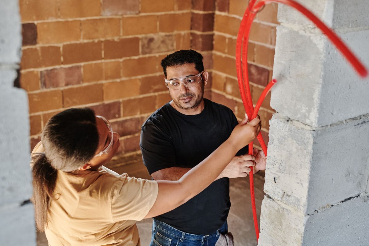 Workers installing electrical wiring on a brick wall